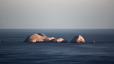 白天，蓝天下蓝色海洋上的褐色岩石形成